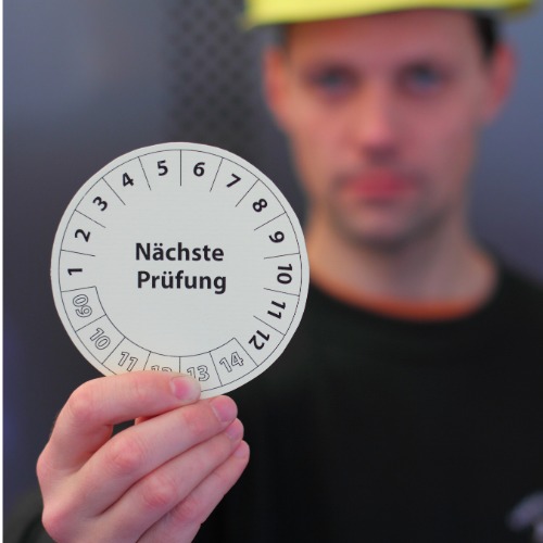 Mitarbeiter hält eine Prüfplakette hoch 