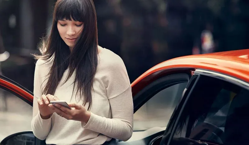 zu sehen ist eine Frau, die am Handy ist vor einem roten Auto