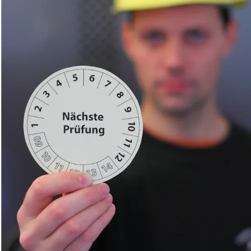 Mitarbeiter hält eine Prüfplakette hoch 